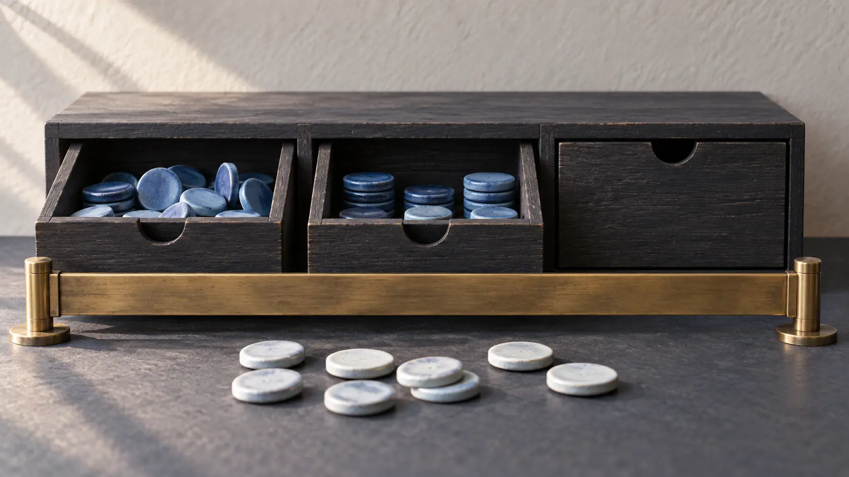 Two open charcoal drawers hold blue ceramic counters beside one closed drawer; a common brass barrier stays lowered before pale counters.