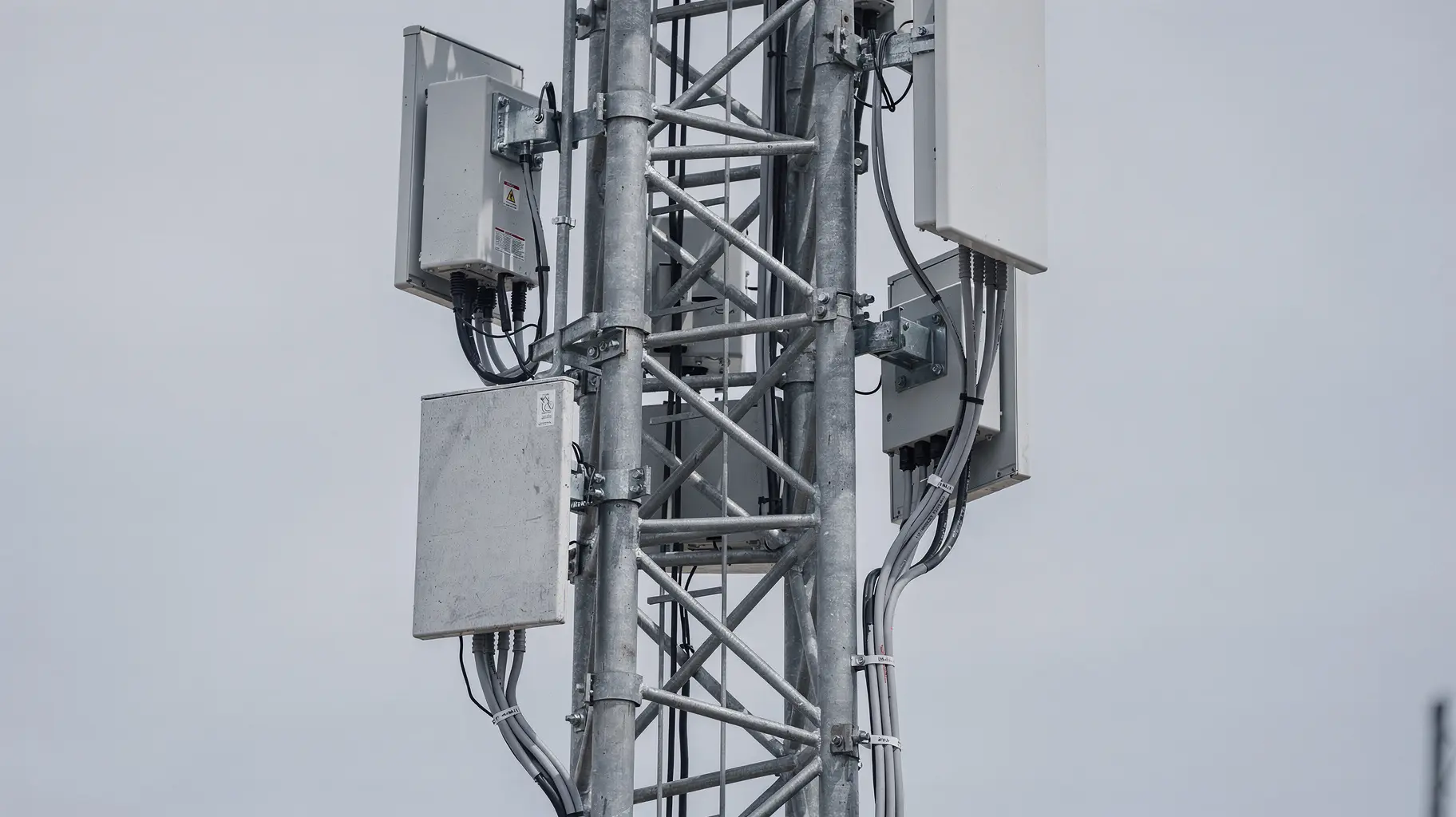 Close view of a steel lattice telecommunications mast filling the frame, with three separate panel antenna mounts bolted to the same structure at three clearly different heights, each on its own steel bracket and each with a grey cable bundle clipped down the galvanised lattice.