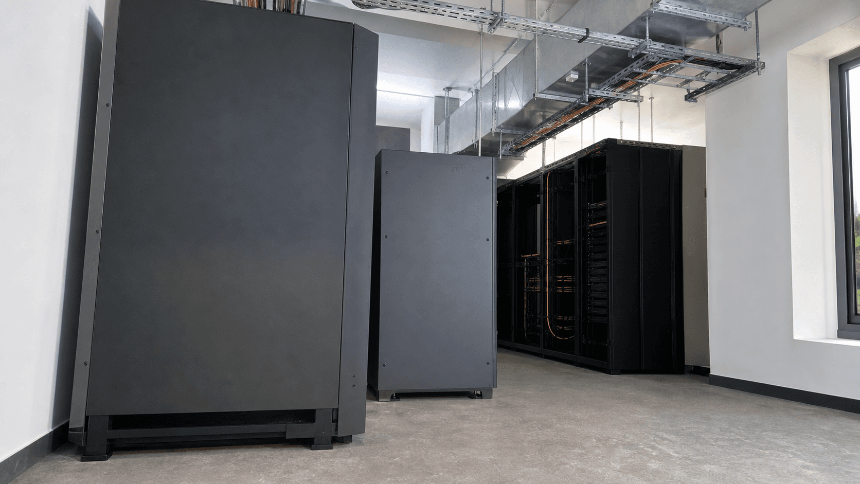 An AI-generated editorial reconstruction shows a compact regional cloud operation in Belagavi, Karnataka: a low, wide corner view of a real-world modest server room led by an unbranded floor-standing UPS or power cabinet, an adjacent cooling unit and overhead cable containment.
